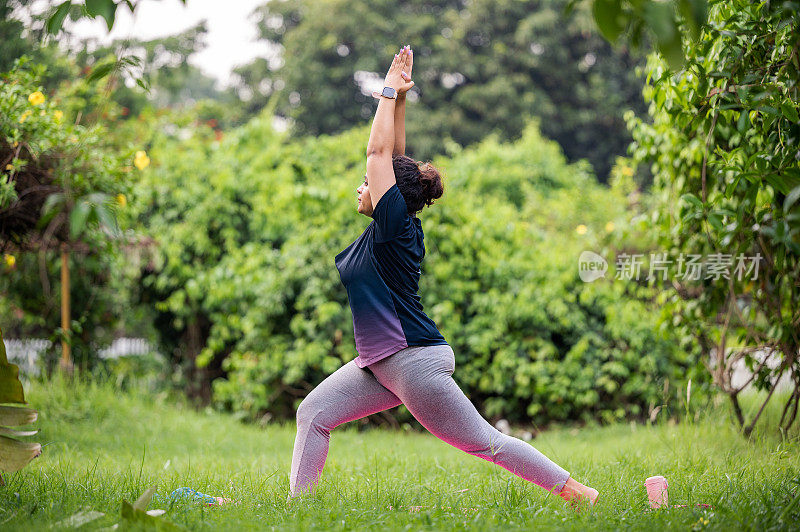 亚洲/印度妇女在公园里练习瑜伽体式，战士1体式或Virabhadrasana I。